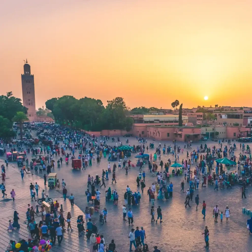 Sunset over Koutoubia Mosque and bustling Jemaa el-Fna square filled with people and lights in Marrakech. Visit Morocco Tours