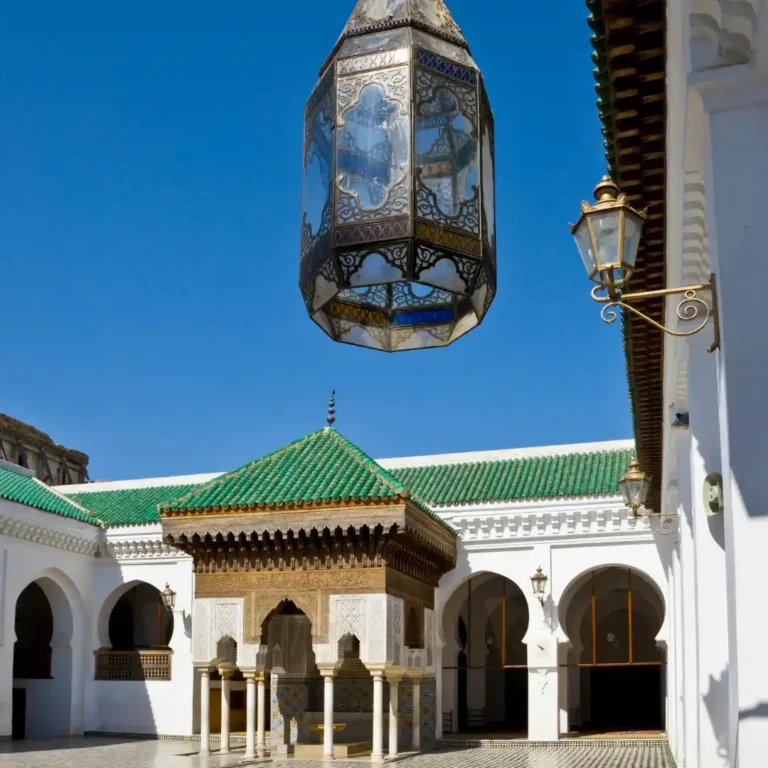 Free Things to Do in Fez | Al Qarawiyyin Courtyard with tiled arcades, carved columns, and the green minaret rising over the old medina. Visit Morocco Tours