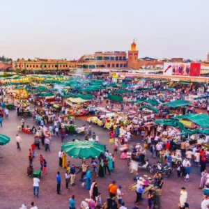 Vibrant daytime scene at Jemaa el-Fnaa square in Marrakech with market stalls. Visit Morocco Tours
