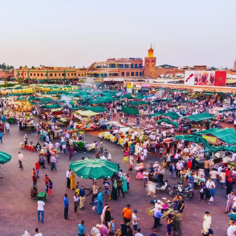 Vibrant daytime scene at Jemaa el-Fnaa square in Marrakech with market stalls. Visit Morocco Tours