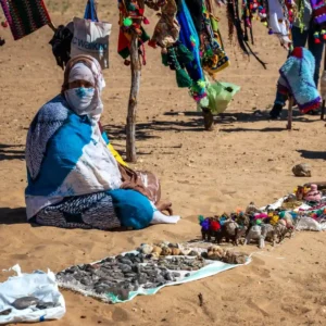 A Berber woman in traditional dress selling handmade souvenirs and crafts at a local market in Morocco. Visit Morocco Tours