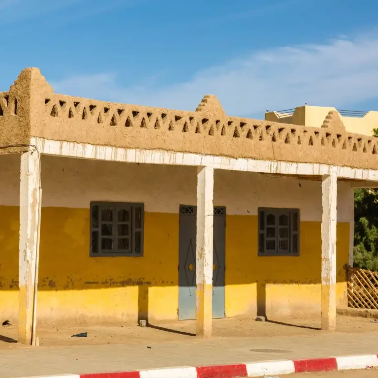 Traditional Berber architecture in Merzouga, showing earthen buildings against the Sahara desert dunes with Visit Morocco Tours.