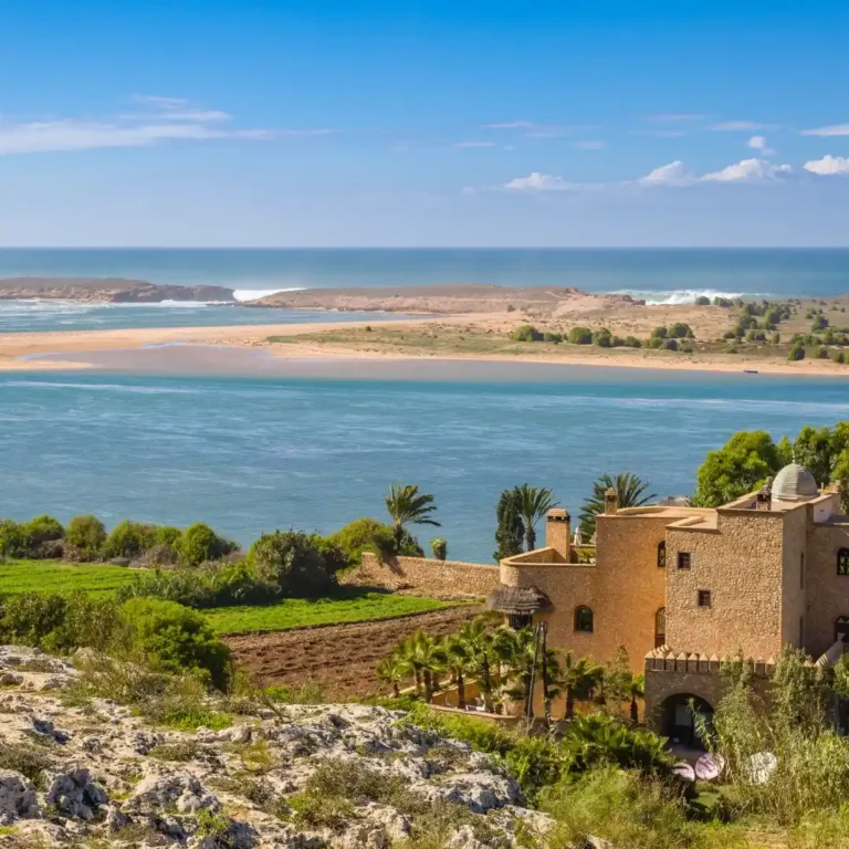 Expansive panoramic view of Oualidia's coastline with traditional fishing boats on the lagoon, Morocco. Visit Morocco Tours